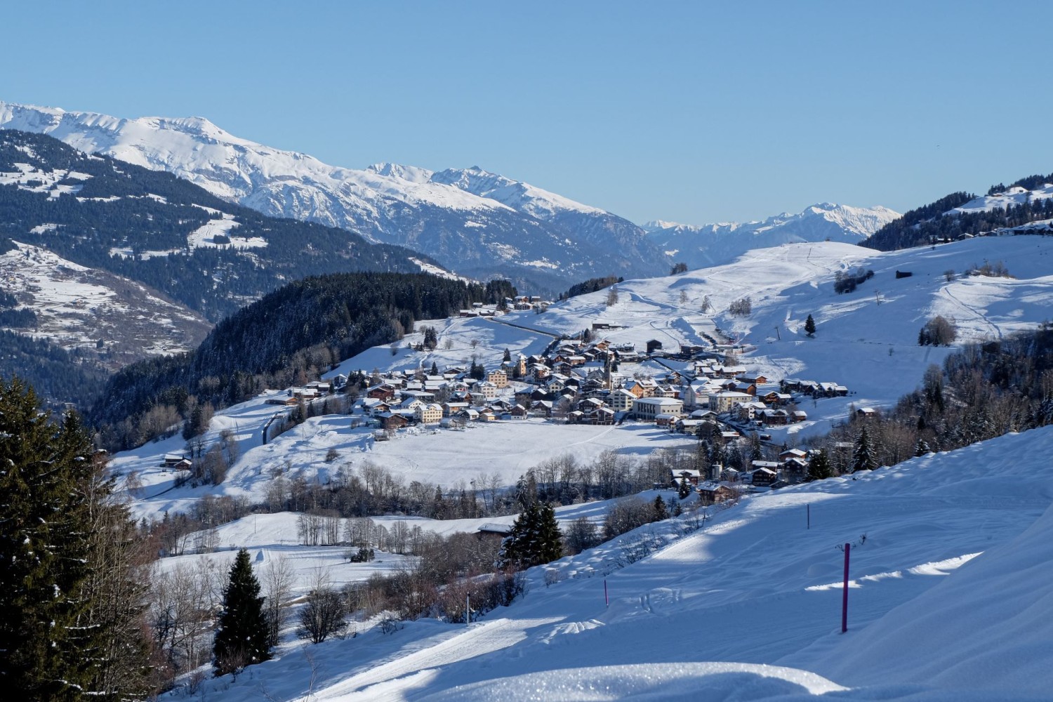 Ein kurzer Blick zurück auf Meierhof, wo die Winterwanderung gestartet ist. Im Hintergrund die Berge der Surselva.